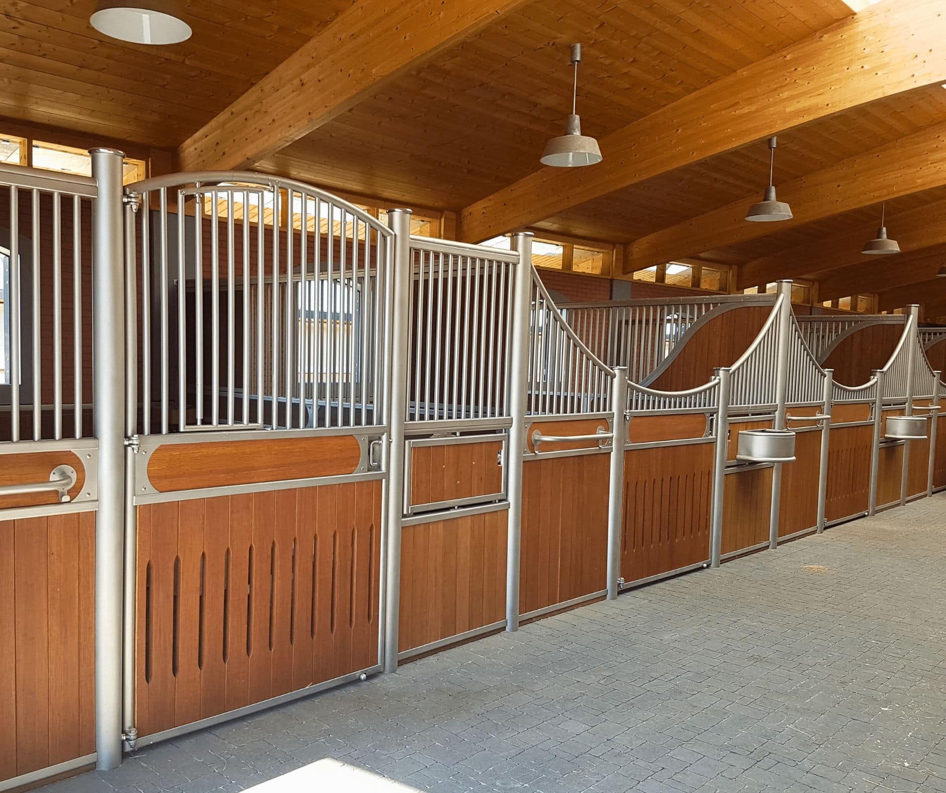 Boxes pour chevaux en bois et métal dans une écurie moderne avec allée pavée